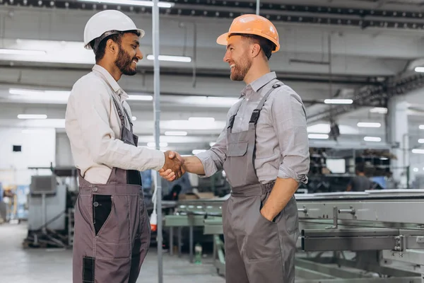两名身穿工作服的国际男工在聚氯乙烯门窗生产的背景下握手 — 图库照片