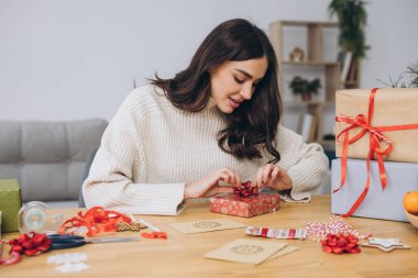 Noel hediyelerini kağıt, makas ve renkli kurdeleler kullanarak örgü ören mutlu kadın. Bayram hazırlıkları..