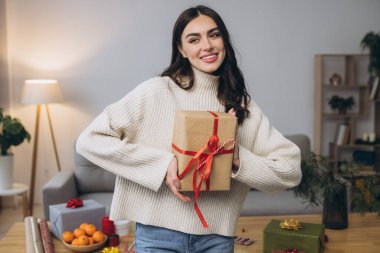 Güzel mutlu kadın evde Noel hediyelerini paketliyor ve tutuyor.