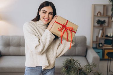 Güzel mutlu kadın evde Noel hediyelerini paketliyor ve tutuyor.
