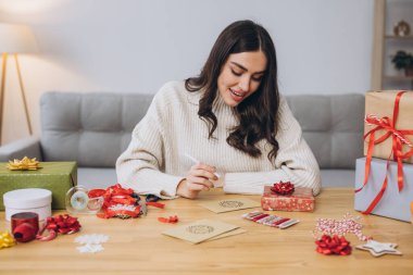 Güzel, mutlu kadın yeni yıl ve Noel için tebrik kartı hazırlıyor ve imzalıyor.