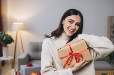 Güzel mutlu kadın evde Noel hediyelerini paketliyor ve tutuyor.