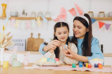 Anne ve kızı yumurta boyuyor. Mutlu aile Paskalya için hazırlanıyor. Tavşan kulağı takan şirin bir kız çocuğu..