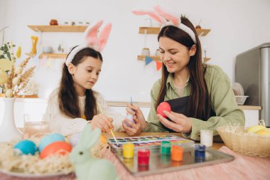 Anne ve kızı yumurta boyuyor. Mutlu aile Paskalya için hazırlanıyor. Tavşan kulağı takan şirin bir kız çocuğu..