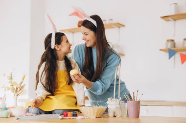 Anne ve kızı yumurta boyuyor. Mutlu aile Paskalya için hazırlanıyor. Tavşan kulağı takan şirin bir kız çocuğu..
