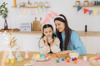 Anne ve kızı yumurta boyuyor. Mutlu aile Paskalya için hazırlanıyor. Tavşan kulağı takan şirin bir kız çocuğu..