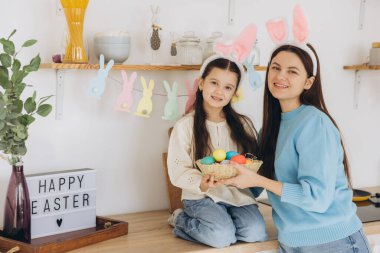 Anne ve kızı renkli yumurta sepeti tutuyorlar. Mutlu aile Paskalya için hazırlanıyor. Tavşan kulağı takan şirin bir kız çocuğu..