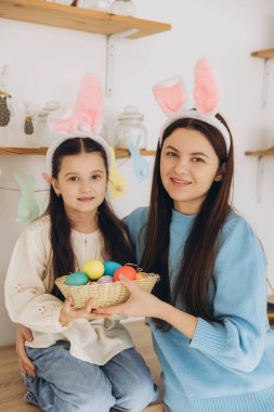 Anne ve kızı renkli yumurta sepeti tutuyorlar. Mutlu aile Paskalya için hazırlanıyor. Tavşan kulağı takan şirin bir kız çocuğu..