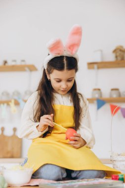 Mutlu Paskalyalar! Dekorayonlarla ve renkli yumurtalarla masada oturan güzel bir kız çocuğu. Paskalya günü tavşan kulağı takan sevimli bir kız çocuğu..
