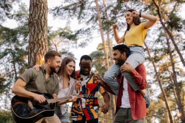 Çok ırklı bir grup insan, sakallı hippi gitar çalıyor ve arkadaşları dans ediyor, şarkı söylüyor ve eğleniyor.