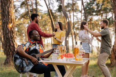 Çok kültürlü insanlar, gitar çalan Afrikalı hippi ve dans eden, şarkı söyleyen ve eğlenen arkadaşlar.