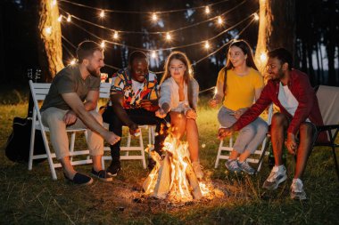 Şenlik ateşinin başında oturmuş marşmelov kızartıyorlar.