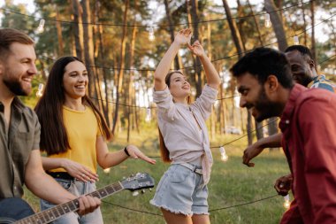 Çok ırklı bir grup, arka planda dans eden güzel hippi bir kadın eğleniyor.