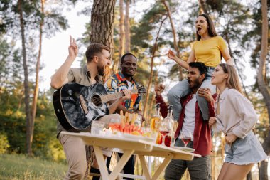 Çok kültürlü bir grup insan, sakallı hippi gitar çalıyor ve arkadaşları dans ediyor, şarkı söylüyor ve eğleniyor.