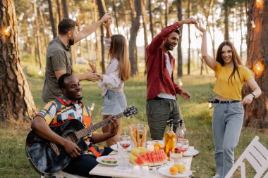 Çok kültürlü insanlar, gitar çalan Afrikalı hippi ve dans eden, şarkı söyleyen ve eğlenen arkadaşlar.