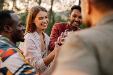 Çok ırklı bir grup mutlu arkadaş masanın etrafında oturur, şarap içer ve yaz ormanlarında akşam yemeği partisinde konuşurlar.