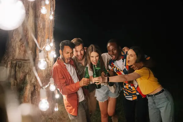 A company of multiracial friends drinking beer at party, making faces near hanging lamps
