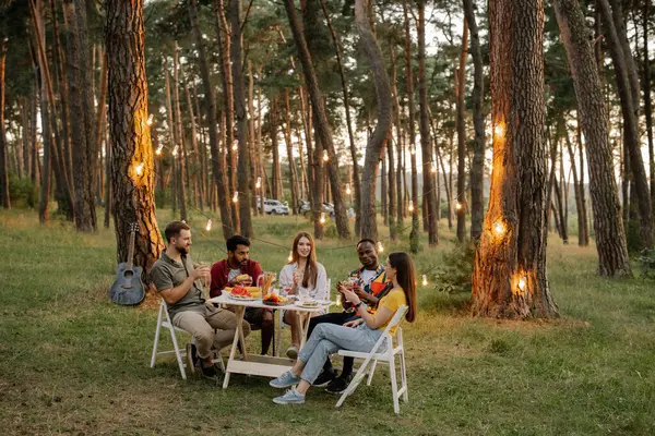 在夏夜森林的晚宴上 一群快乐的朋友围坐在桌旁喝酒聊天 — 图库照片