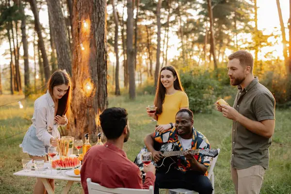 Multiracial group of friends, African man playing guitar around happy friends drinking wine