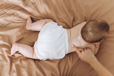 Mutlu anne bebeğinin vücuduna krem sürüyor.