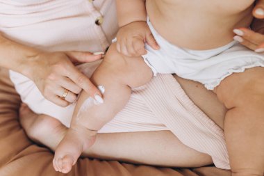 Mutlu anne bebeğinin vücuduna krem sürüyor.