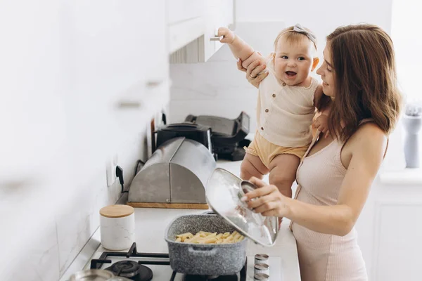 彼女の小さな赤ちゃんの娘と母親はキッチンで食べ物を準備する — ストック写真