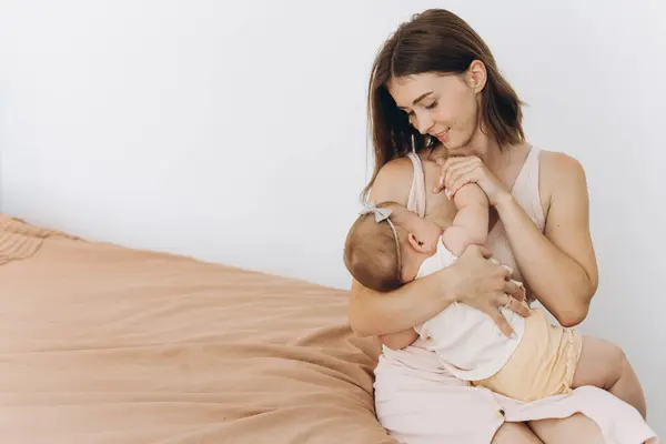 明るい部屋のベッドで赤ん坊の女の子を授乳する幸せな母親 — ストック写真