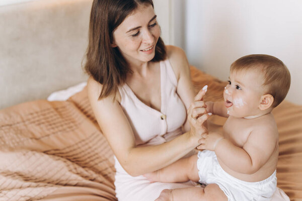 Счастливая мать наносит крем на тело и лицо своей малышки