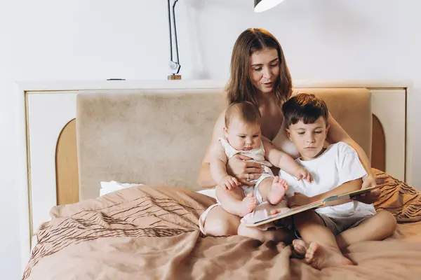 A young mother reads a fairy tale to her children, a boy and a little baby girl