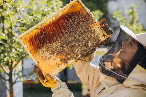 Szczęśliwa Uśmiechnięta Pszczelarka Mundurze Stojąca Pasiece Trzymająca Ramę Pszczoły Miodnej — Zdjęcie stockowe
