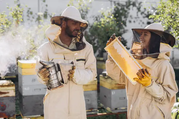 蜂の農場の養蜂場の近くで養蜂用具を使用している幸せな微笑みの養蜂家のカップル — ストック写真