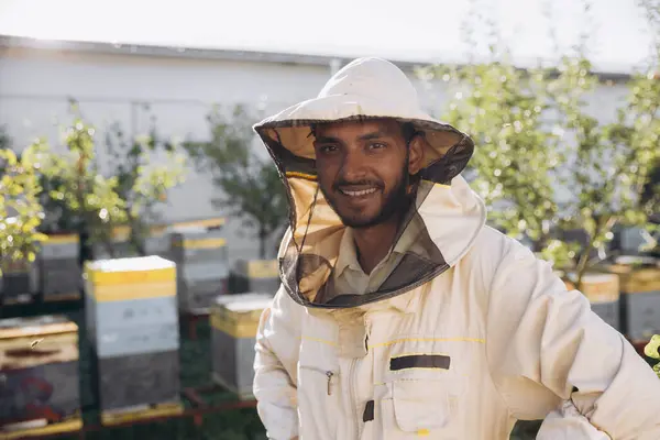 Portrait of a happy Indian male beekeeper working in an apiary near beehives with bees. Collect honey. Beekeeper on apiary. Beekeeping concept.