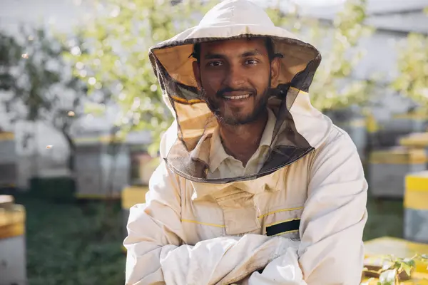 Portrait of a happy Indian male beekeeper working in an apiary near beehives with bees. Collect honey. Beekeeper on apiary. Beekeeping concept.