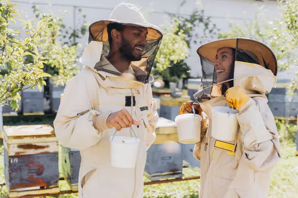 Happy smiling international couple of beekeepers holds ready organic honey made on a bee farm
