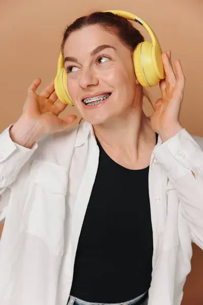 Moderní Žena Usmívá Rovnátka Zubech Poslouchá Hudbu Sluchátkách Béžovém Pozadí Stock Obrázky