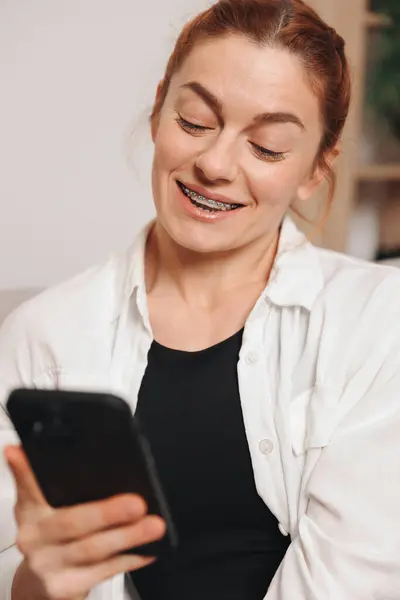 Portret Dojrzałej Uśmiechniętej Kobiety Aparatem Zęby Smartfonem Domu Obrazy Stockowe bez tantiem