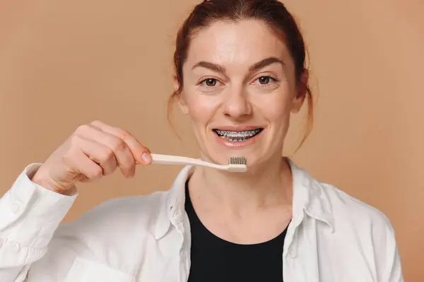 ベージュの背景に歯ブラシを保持するブレースで幸せな成熟した女性 ストック画像