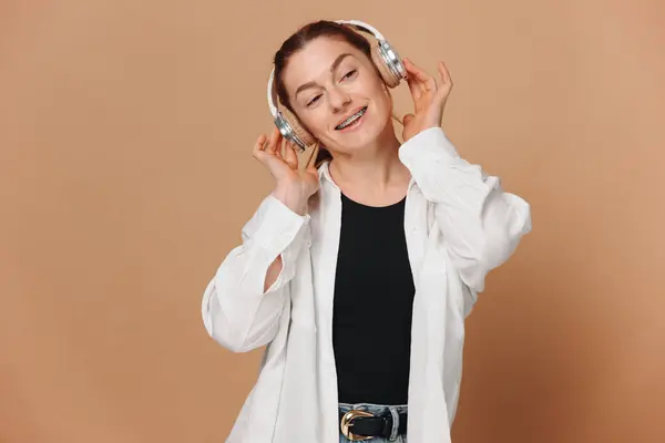 Moderní Žena Usmívá Rovnátka Zubech Poslouchá Hudbu Sluchátkách Béžovém Pozadí Stock Snímky