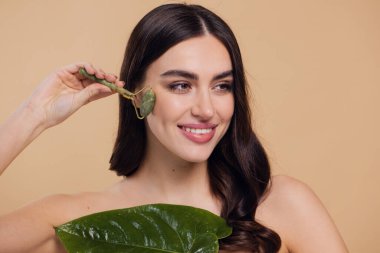 Mükemmel ciltli güzel bir kadının yarı çıplak portresini kapat. Bej arka planda doğal kuvars taşıyla yüz masajı yap..