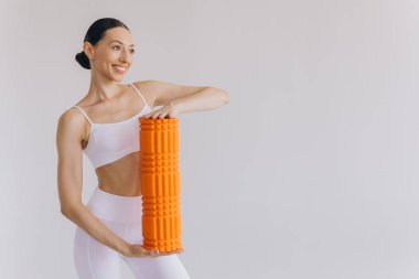 Beyaz spor giysili güzel, ince kadın spor kıyafetleri içinde, spor salonu için turuncu köpük silindirli, fotokopi alanlı beyaz poz veren, sağlığını ve sağlığını destekleyen,.