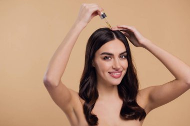 Bej arka planda saç köklerine gerekli yağı uygulayan mutlu genç kadının güzel portresi, metin için boşluk