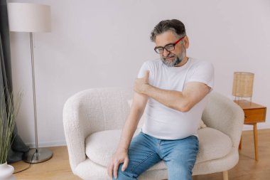 Artrit belirtileri. Evde omuz ağrısı çeken yaşlı sakallı adam.