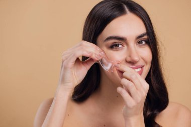 Göz bantları. Güzellik konsepti. Güzel bir model gözlerine pembe hidro jel sürerek bej arka planda gülümsüyor.