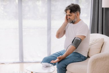 Evdeki kanepede oturmuş, tansiyonunu ölçen, gri saçlı, son sınıf öğrencisi. Modern tonometre kullanan emekli, hipertansiyon deneyimi yaşayan, kopyalama alanı