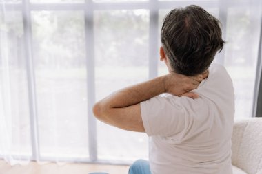 Üst sınıflardan biri içeride oturuyor, boynu ağrıyormuş gibi görünüyor. Üzüntülü bir ifadeyle boynunu tutuyor, rahatsız olduğunu gösteriyor..