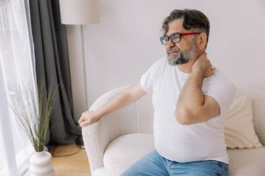 Üst sınıflardan biri içeride oturuyor, boynu ağrıyormuş gibi görünüyor. Üzüntülü bir ifadeyle boynunu tutuyor, rahatsız olduğunu gösteriyor..