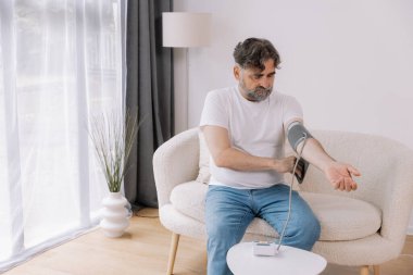Evdeki kanepede oturmuş, tansiyonunu ölçen, gri saçlı, son sınıf öğrencisi. Modern tonometre kullanan emekli, hipertansiyon deneyimi yaşayan, kopyalama alanı