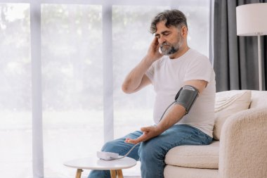 Evdeki kanepede oturmuş, tansiyonunu ölçen, gri saçlı, son sınıf öğrencisi. Modern tonometre kullanan emekli, hipertansiyon deneyimi yaşayan, kopyalama alanı