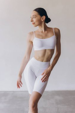 Zayıf vücutlu genç bir kadın gri duvarda yoga yapıyor. Sağlıklı yaşam ve zihinsel gelişim arasındaki doğal denge kavramı.