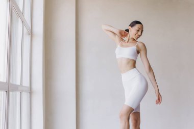 Zayıf vücutlu sportif genç bir kadın, panoramik pencereli modern odada yoga pratiği yapıyor. Vücut ve zihinsel gelişim arasındaki sağlıklı yaşam ve doğal denge kavramı.